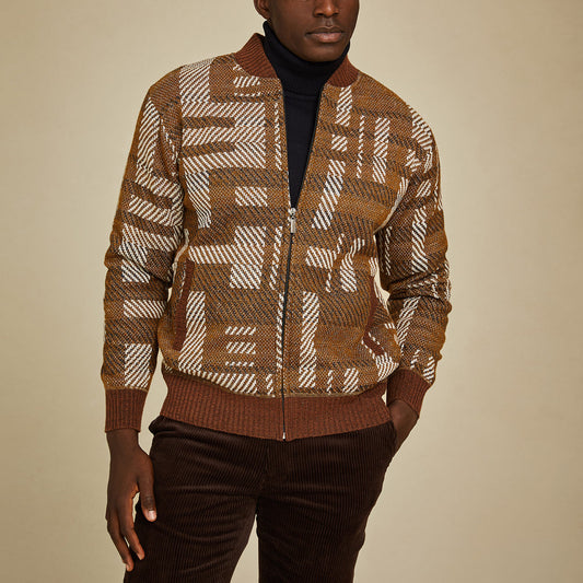 A man wears the Inserch Geometric Full Zip Baseball Knit Jacket SW609-27 Aztec over a black turtleneck and brown corduroy pants, standing against a plain beige background.