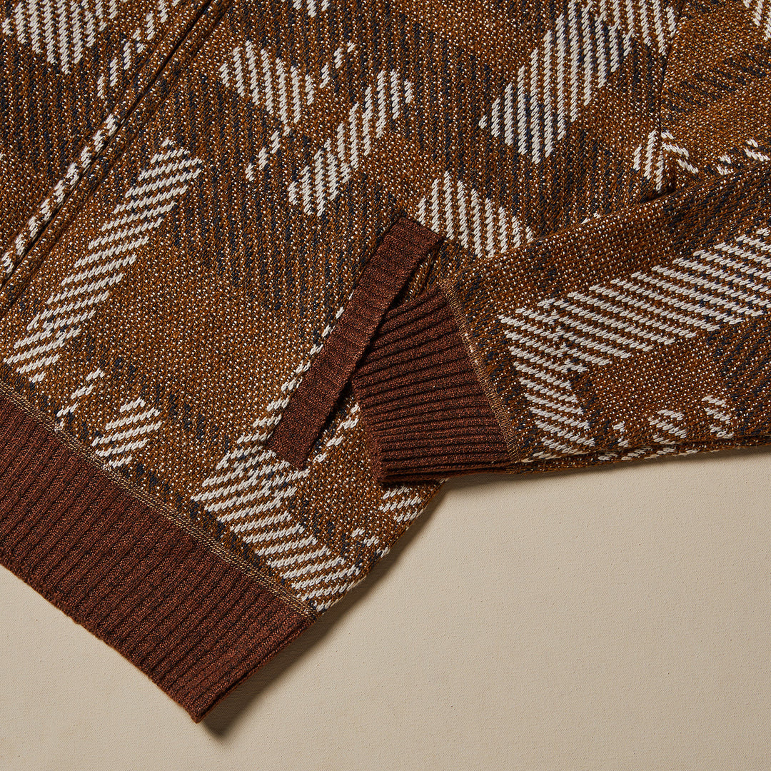 A man wears the Inserch Geometric Full Zip Baseball Knit Jacket SW609-27 Aztec over a black turtleneck and brown corduroy pants, standing against a plain beige background.