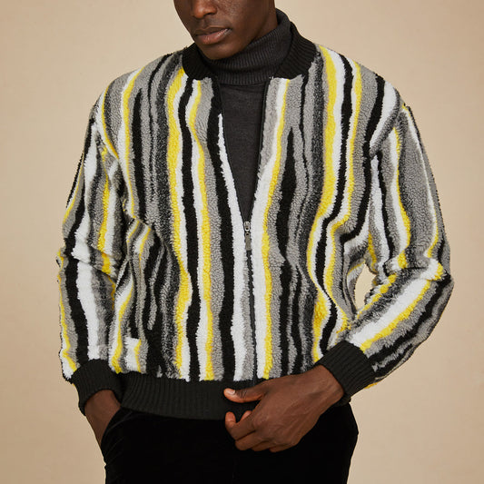 A man stands against a beige background wearing the Inserch Faux Sherpa Stripe Baseball Sweater Jacket SW610-01 Black, featuring vertical black, white, gray, and yellow stripes.