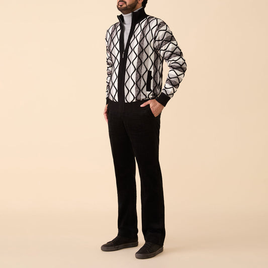 A man stands against a beige background wearing the Inserch Bouclé Yarn Graphic Full Zip Sweater (SW614-00001) in black, paired with a light gray turtleneck, black pants, and dark shoes.