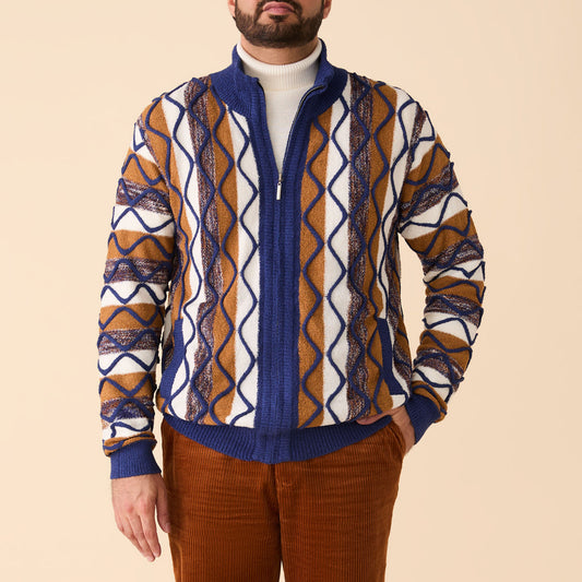 A man stands against a beige background wearing an Inserch Bouclé Yarn Graphic Full Zip Sweater SW614-00013 Royal Blue, a white mockneck turtleneck, and brown corduroy pants.