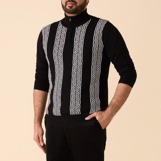 A man wears the Inserch Grecian Intarsia Half Zip Sweater SW615-00001 Black with white Greek key patterns and black pants, standing with one hand in his pocket against a plain beige background.