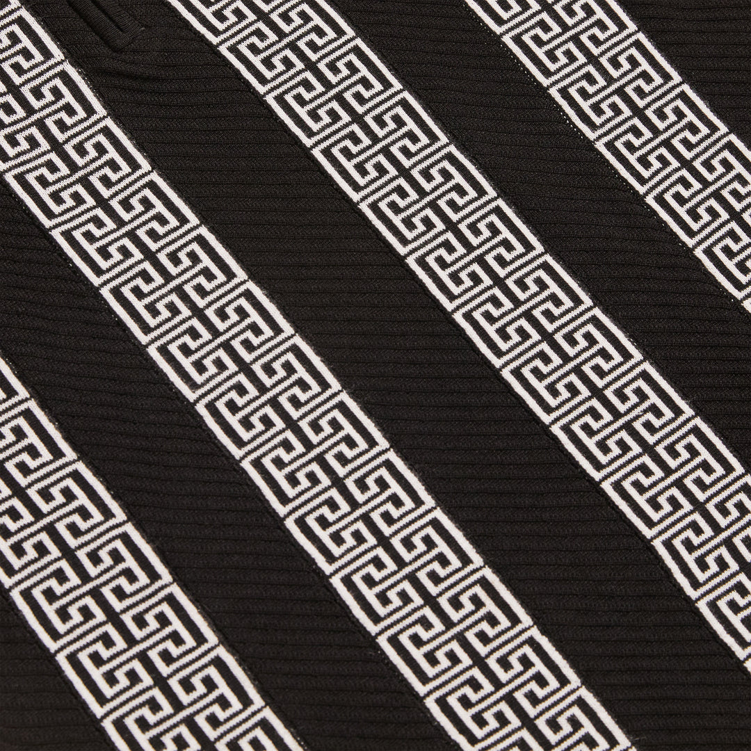 A man wears the Inserch Grecian Intarsia Half Zip Sweater SW615-00001 Black with white Greek key patterns and black pants, standing with one hand in his pocket against a plain beige background.