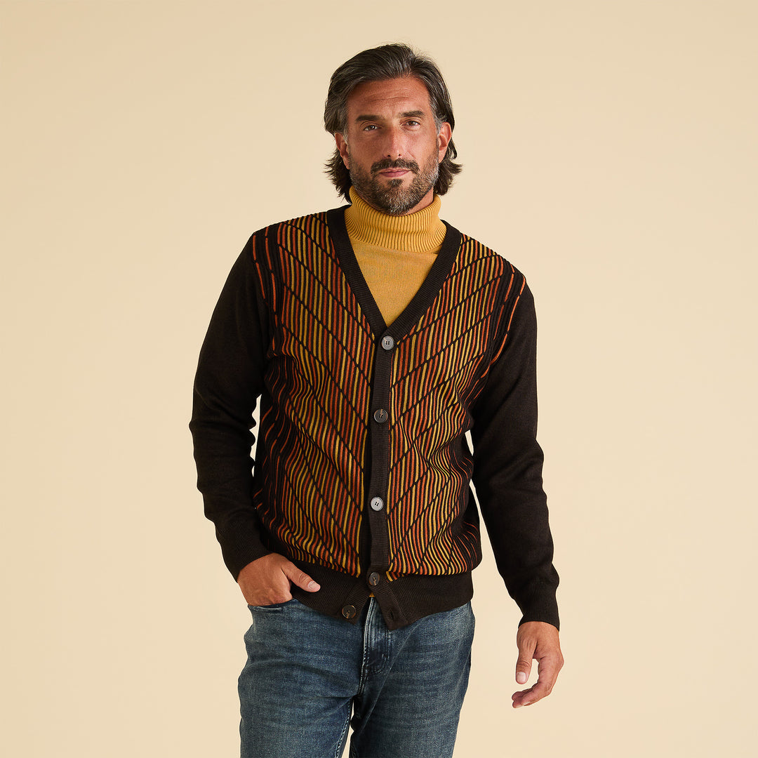 A man in an Inserch Intarsia Panel Cardigan SW904-24 Chocolate stands against a plain beige background, wearing a yellow turtleneck beneath the geometric-patterned sweater.