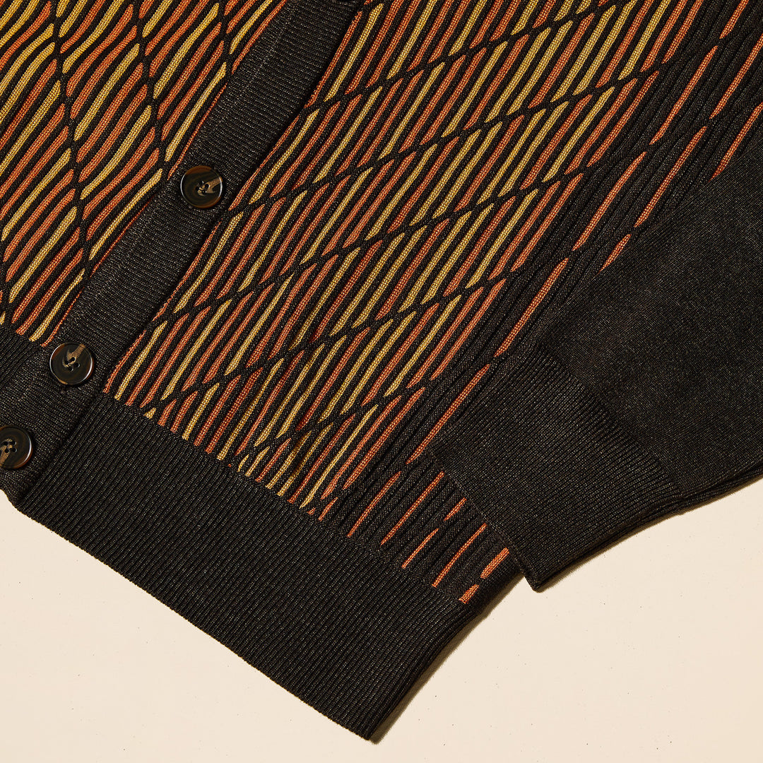 A man in an Inserch Intarsia Panel Cardigan SW904-24 Chocolate stands against a plain beige background, wearing a yellow turtleneck beneath the geometric-patterned sweater.