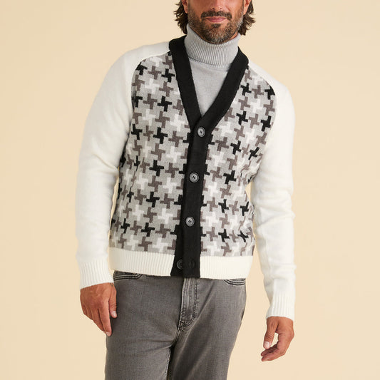 A man wears the Inserch Houndstooth Pattern Cardigan SW906-41 Black/White by Inserch, featuring black buttons and a black and gray cross pattern, styled with a light gray turtleneck and gray jeans against a beige background.