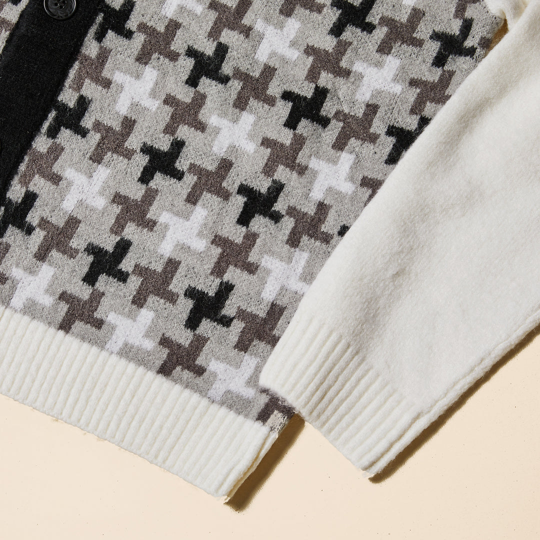 A man wears the Inserch Houndstooth Pattern Cardigan SW906-41 Black/White by Inserch, featuring black buttons and a black and gray cross pattern, styled with a light gray turtleneck and gray jeans against a beige background.