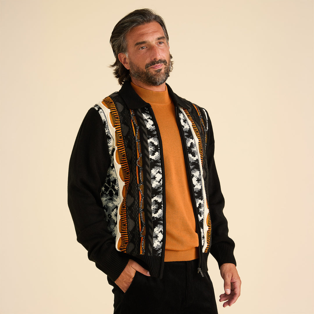 A man wears the Inserch 3D Intarsia Full Zip Sweater SW907-01 in black, featuring orange and white vertical stripes, over a rust shirt against a beige background. Brand: Inserch. Final sale, size L only, in store.