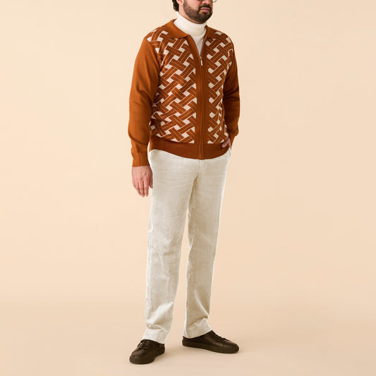 A man stands against a beige background in the Inserch Geometric Full Zip Sweater SW908-00005 Caramel, paired with a white turtleneck, light beige pants, and dark brown shoes. His face is partially out of frame.