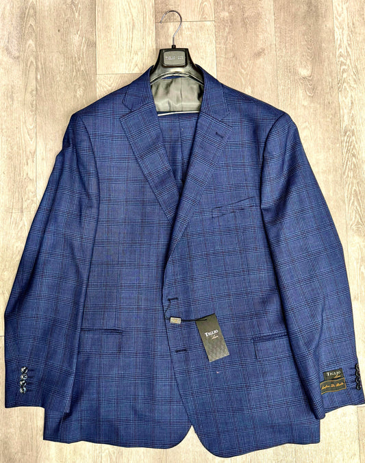 A Tiglio Luxe Dolcetto Modern Fit, Pure Wool Suit 332213/901 jacket in a blue checkered pattern, made from Italian fabrics, hangs elegantly on a wooden hanger with its tag attached, displayed on a wooden floor. This piece embodies timeless sartorial traditions.