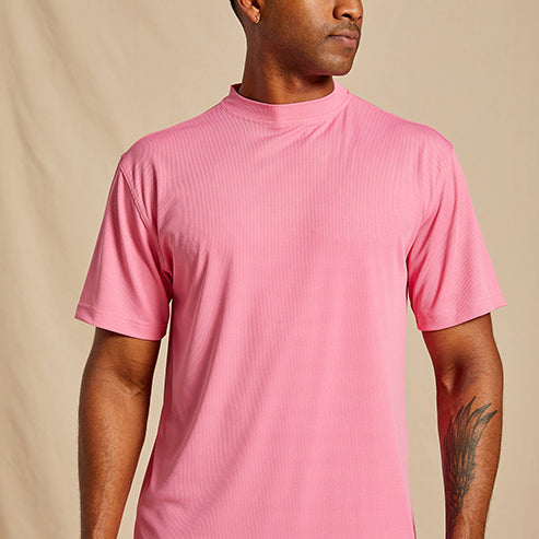 A man wears the Inserch Rib Crew Neck T-Shirt T299-00057 in Summer Pink from Inserch, made of a soft polyester-spandex blend, standing against a beige background and facing slightly to the side.