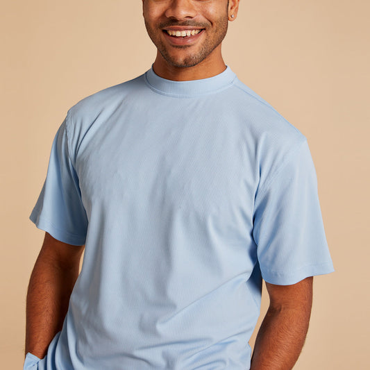 A person wearing the Inserch Rib Crew Neck T-Shirt T299-00154 Lake Blue by Inserch stands against a beige background, smiling with one hand in their pocket.