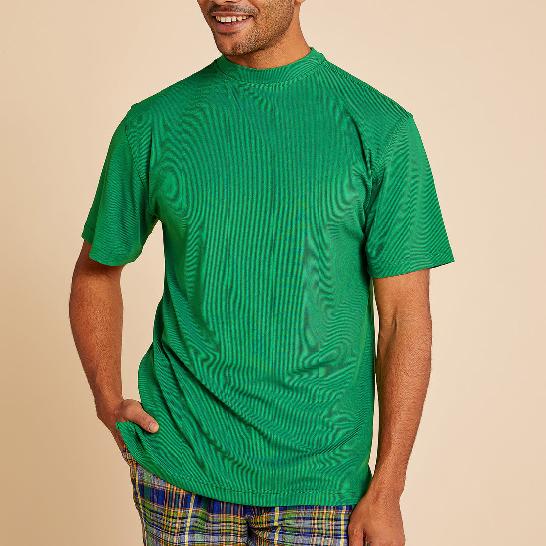 A person wearing the Inserch Rib Crew Neck T-Shirt T299-00200 Emerald by Inserch and plaid pants stands against a beige background, with one hand in their pocket.