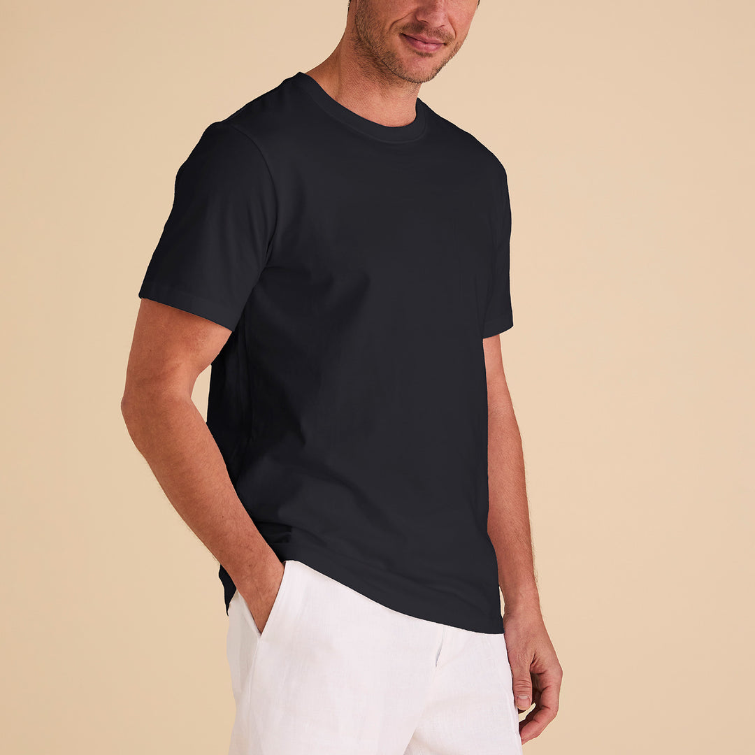 A man models the Inserch Short Sleeve Pima Cotton T-Shirt T301-00001 in black, paired with white pants against a light beige background, hand in pocket, highlighting the regular fit style.