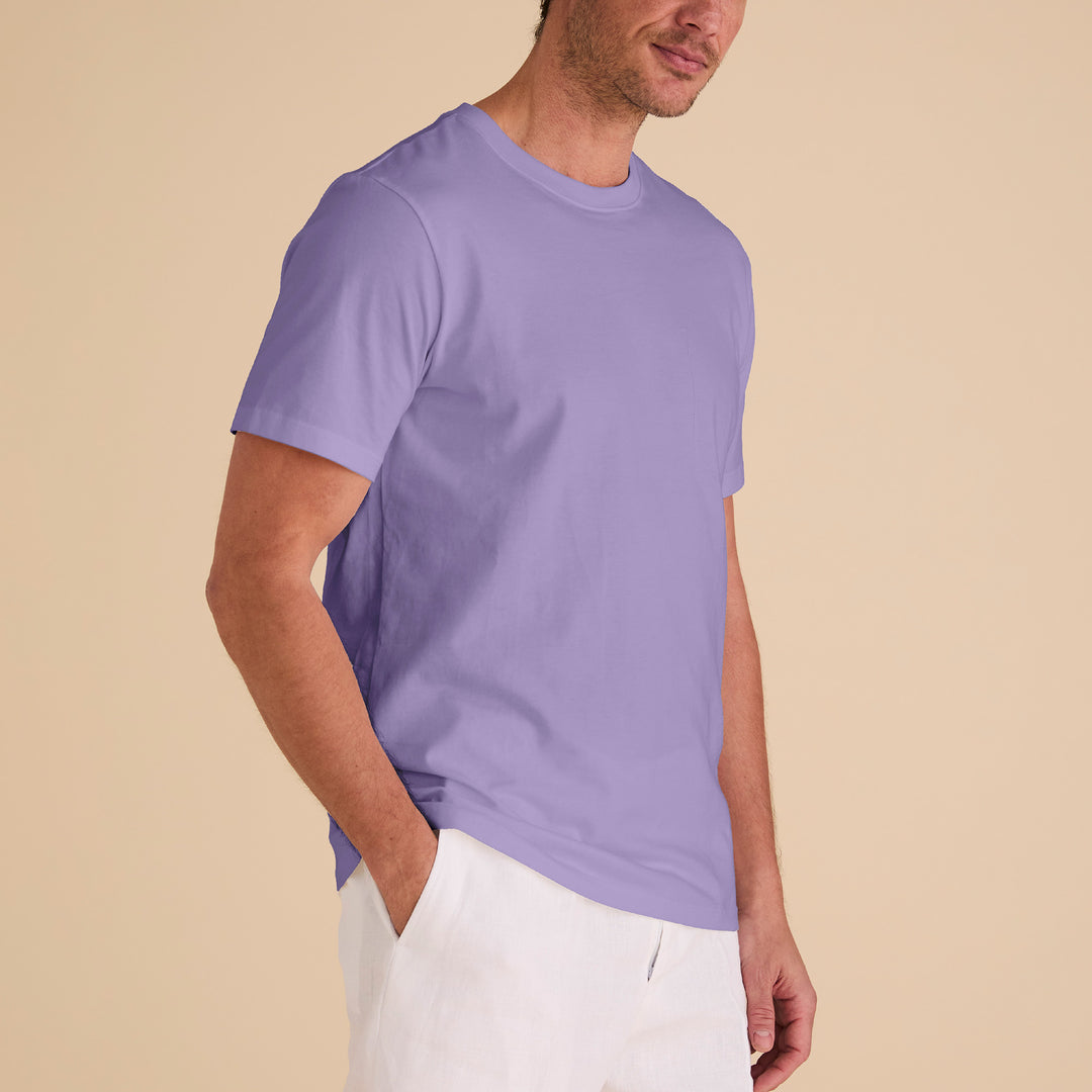 A person wearing an Inserch Short Sleeve Pima Cotton T-Shirt T301-00119 in lavender and white pants stands against a beige background, with hands in pockets, gazing to the side.
