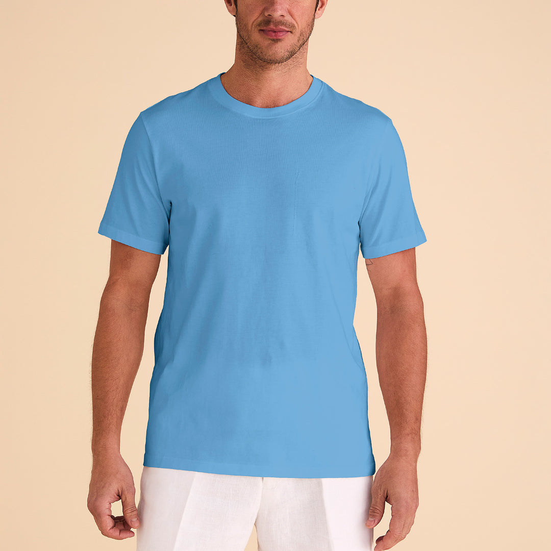 A man wearing an Inserch Short Sleeve Pima Cotton T-Shirt T301-00183 Blue Mist and white pants stands against a beige background.