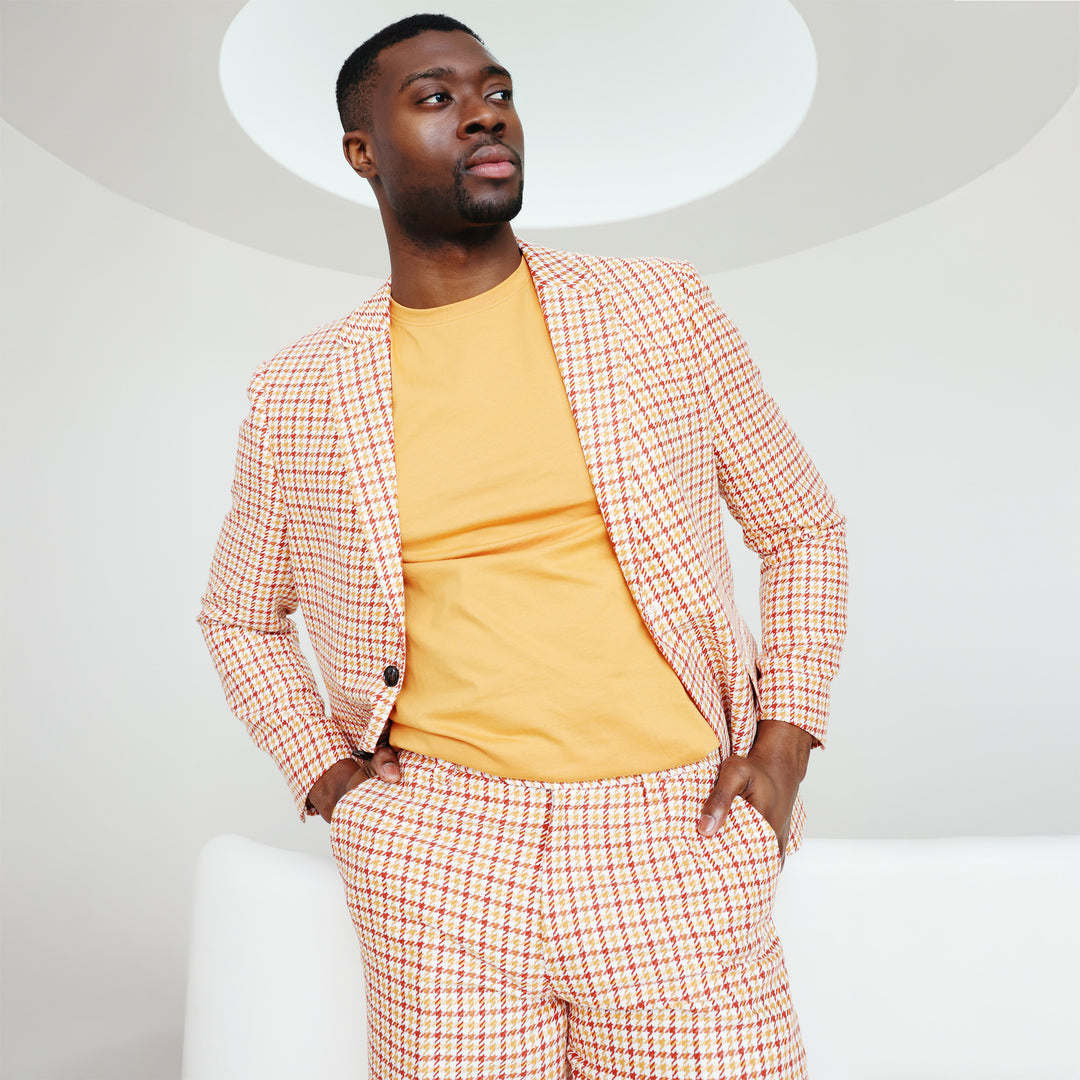 A man wearing the Inserch Short Sleeve Pima Cotton T-Shirt T301-00191 Sunburst and white pants stands against a beige background, smiling while holding his shirt's edge.