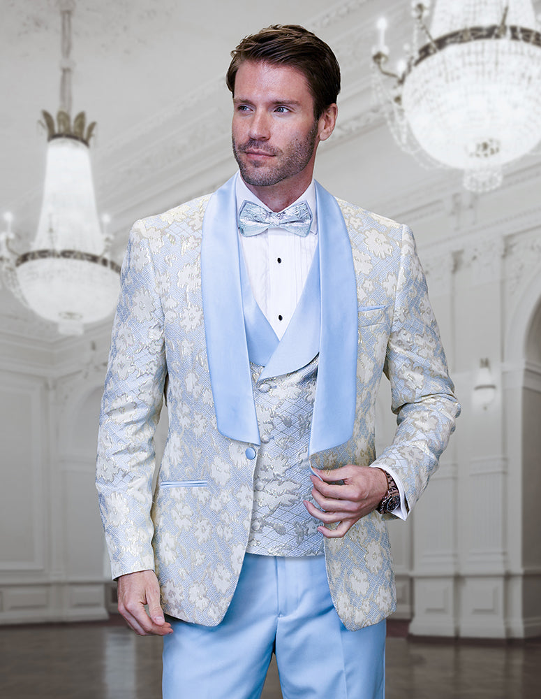 A man in the STATEMENT CLOTHING | TIZANO-SKYBLUE modern fit tuxedo from Statement Clothing, complete with a matching vest and bow tie, stands in an elegant, chandelier-lit ballroom.