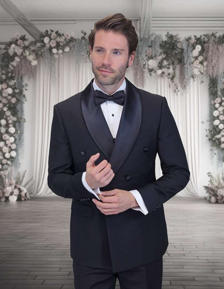 A man wears the STATEMENT CLOTHING | TUX-DBS-BLACK by Statement Clothing, a modern fit black tuxedo with a bow tie, standing before a white floral backdrop and draped curtains. A hint of sky blue adds a subtle contemporary accent to his look.
