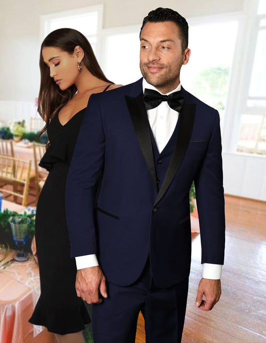 A man in the STATEMENT CLOTHING | TUX-PK-NAVY by Statement Clothing stands in front of a woman in a black dress inside a decorated room with tables and chairs.