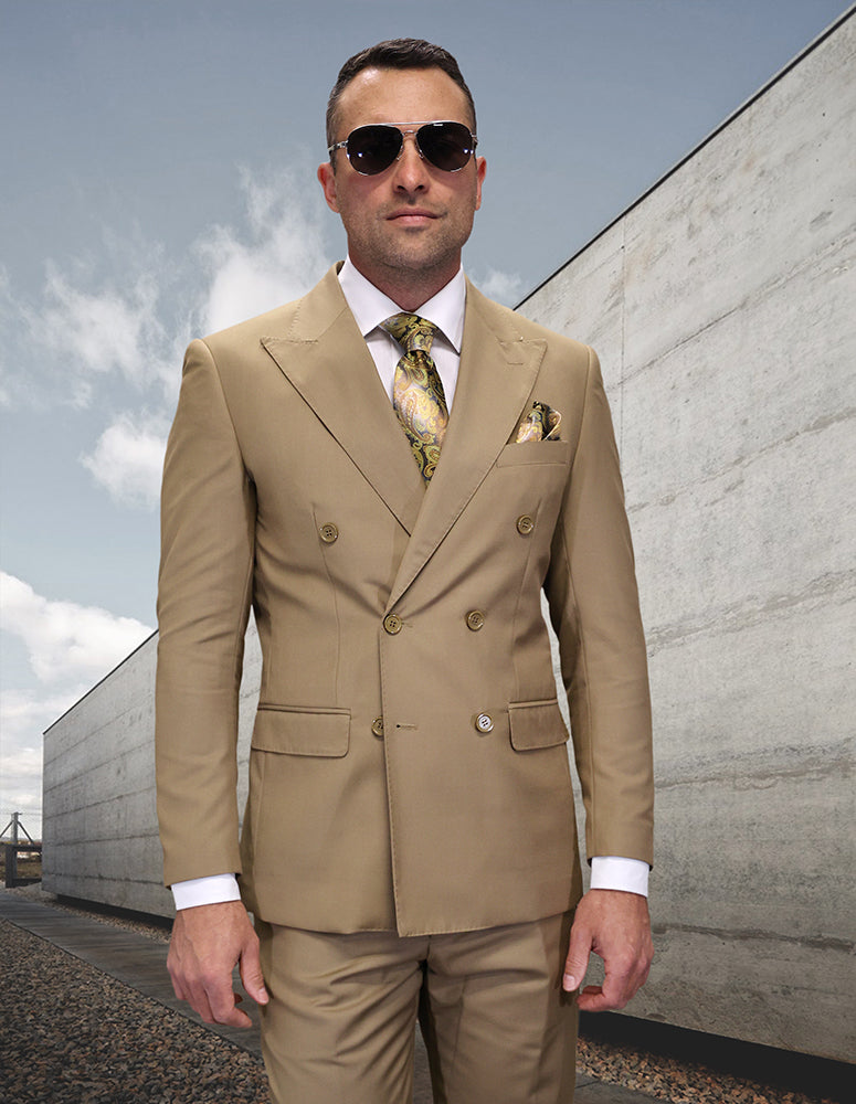A man wearing the Statement Clothing TZD-100-CARAMEL modern fit double-breasted tan Italian wool suit, with a white shirt, patterned tie, and sunglasses, stands outdoors by a concrete wall.