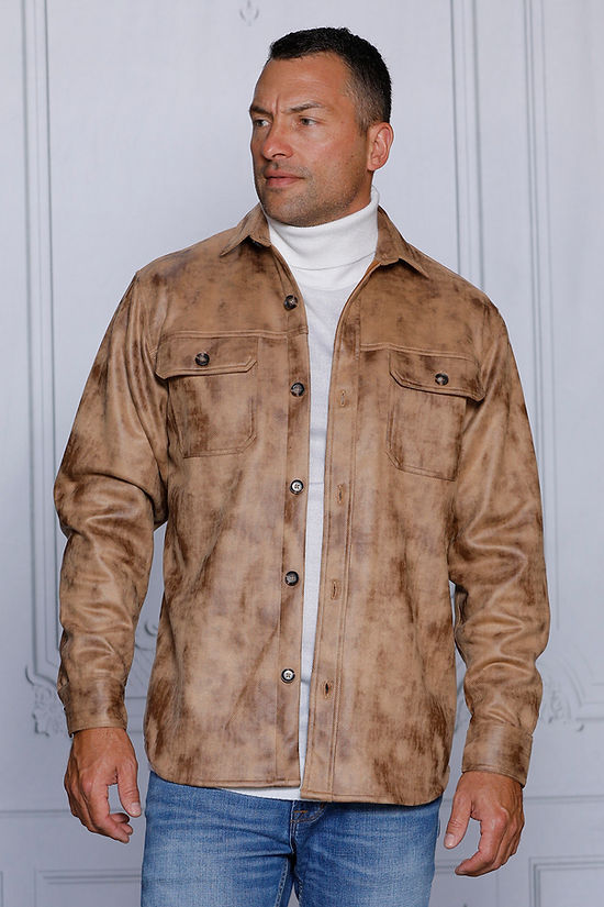 A man is wearing the MANZINI VALENTINO Camel Soft Vegan Suede Button Sweater Shirt by Insomnia over a white turtleneck and blue jeans, standing indoors against a plain wall.