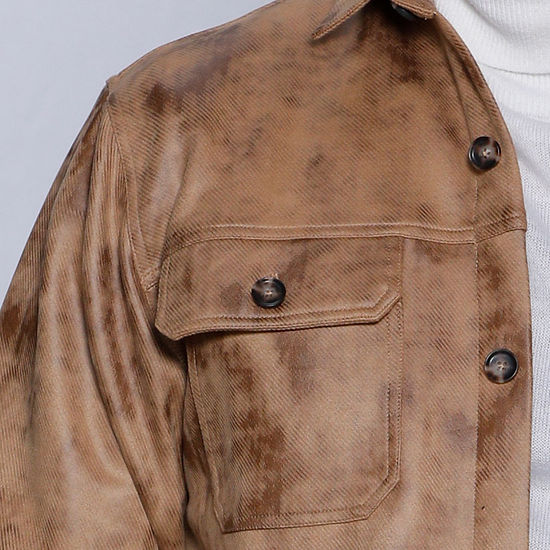 A man is wearing the MANZINI VALENTINO Camel Soft Vegan Suede Button Sweater Shirt by Insomnia over a white turtleneck and blue jeans, standing indoors against a plain wall.