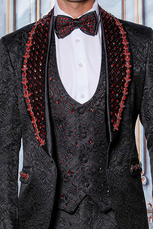 A man poses against ornate moldings in an Insomnia MANZINI ZARA 3-piece slim fit tuxedo, featuring a black/red floral pattern with rhinestone trim, and a bow tie.