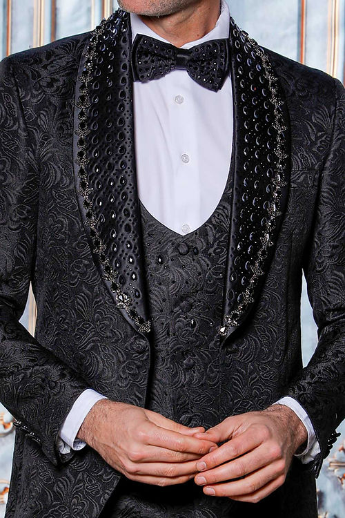 A man wearing an Insomnia MANZINI ZARA 3-Piece Slim Fit Rhinestone Floral Pattern Black Tuxedo Suit and a bow tie stands before a decorative backdrop.