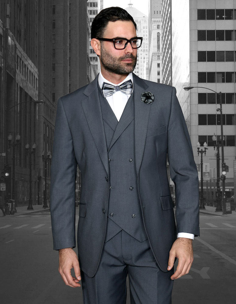 A man in the STATEMENT CLOTHING | ZARGALA-CHARCOAL Italian wool suit by Statement Clothing, with a white shirt and bow tie, stands on a city street with tall buildings in the background, showcasing its modern fit.
