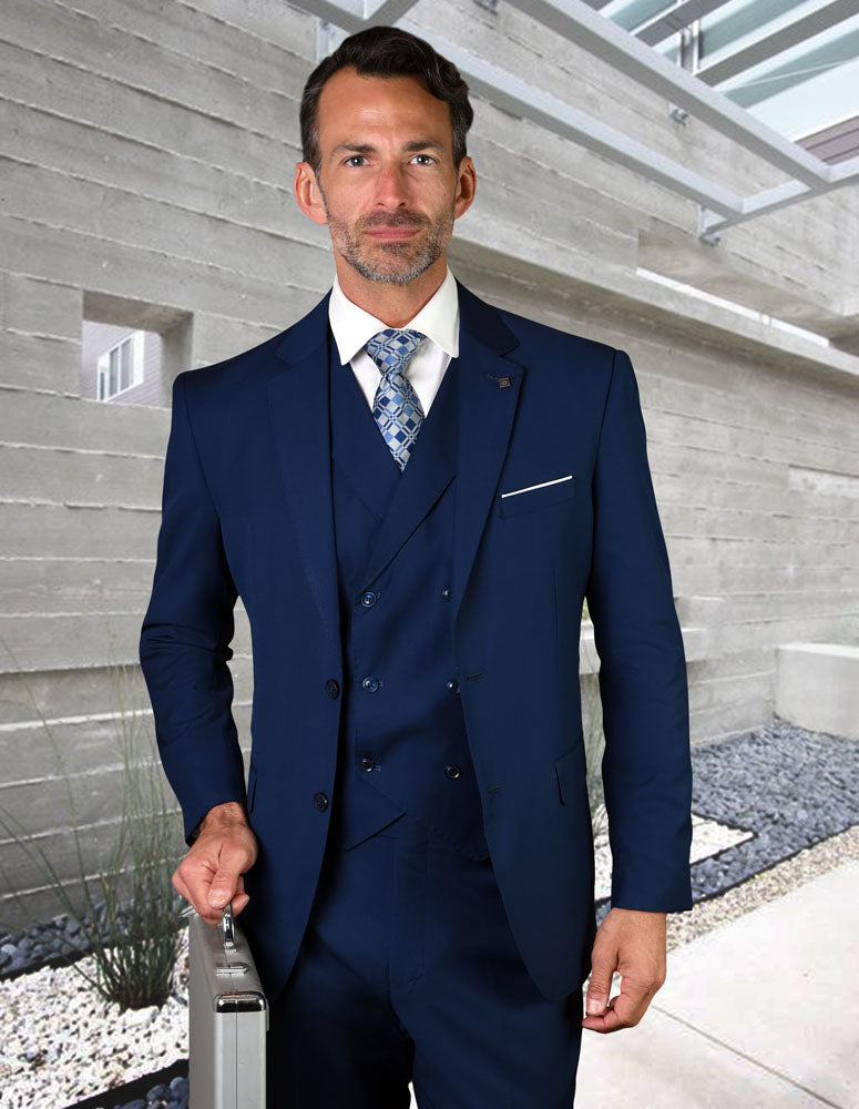 A man in the STATEMENT CLOTHING | ZARGALA-SAPPHIRE modern fit suit by Statement Clothing, featuring an Italian wool double-breasted vest, holds a silver briefcase and stands outdoors amidst concrete walls and landscaping.
