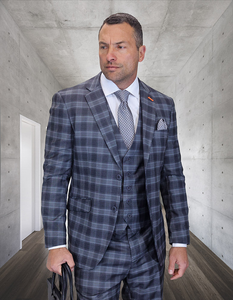 A man stands in a modern hallway, holding a black bag and wearing the STATEMENT CLOTHING | ZILO-1-CHARCOAL suit by Statement Clothing: a gray plaid Italian wool suit with flat front pants and tie.