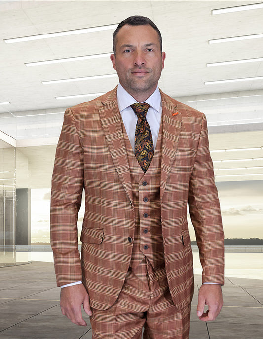 A man in the STATEMENT CLOTHING | ZILO-1-RUST modern fit Italian Super 200’s wool suit by Statement Clothing, paired with a white shirt and patterned tie, stands indoors against a sleek, minimalist background.