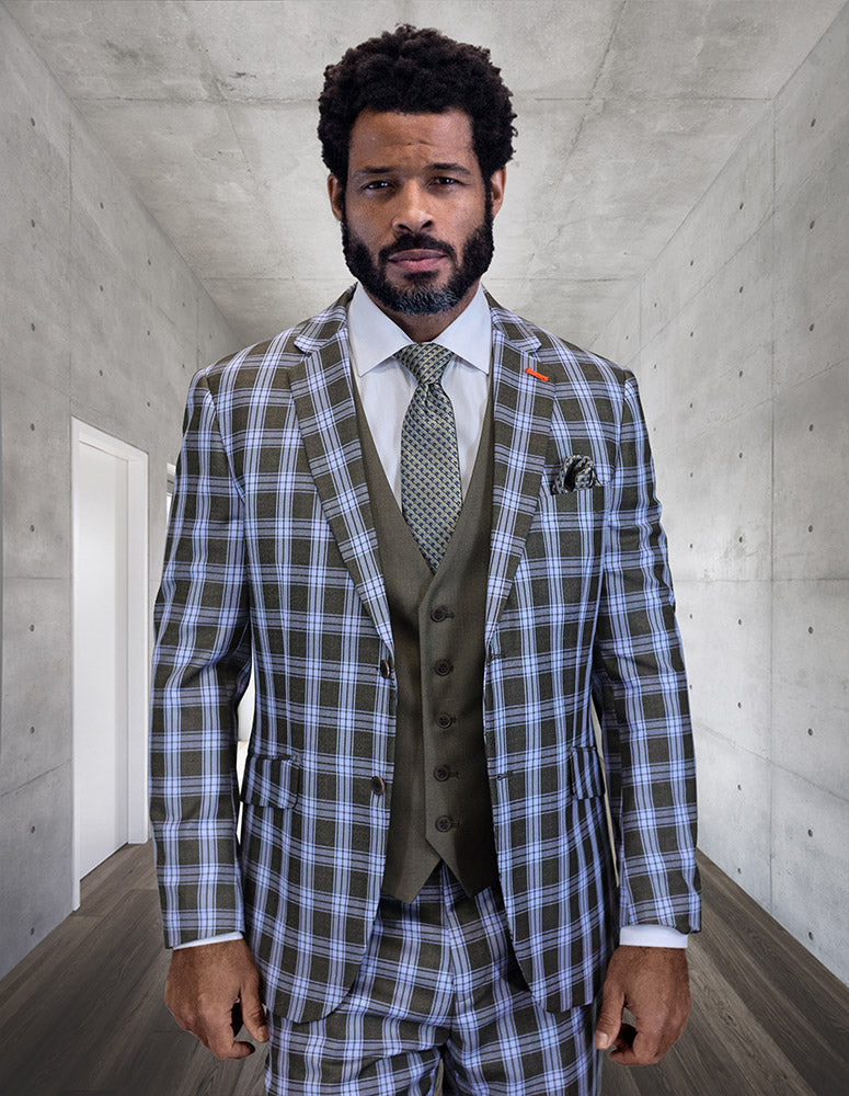 A bearded man stands in a concrete hallway, wearing the STATEMENT CLOTHING | ZILONI-1-BLUE tailored plaid suit with flat front pants, matching vest, white shirt, and tie by Statement Clothing.