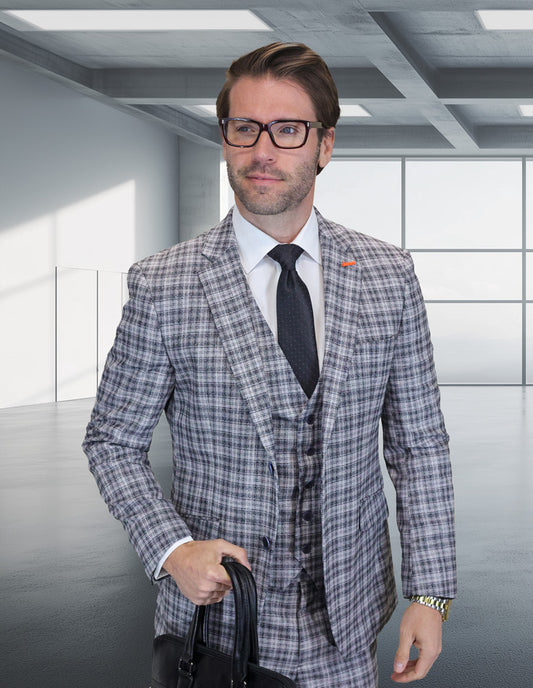 A man in a Statement Clothing ZILONI-4-BLACK Modern Fit Italian Super 200's Wool Suit, white shirt, and black tie stands in a modern, empty office space, holding a black bag.