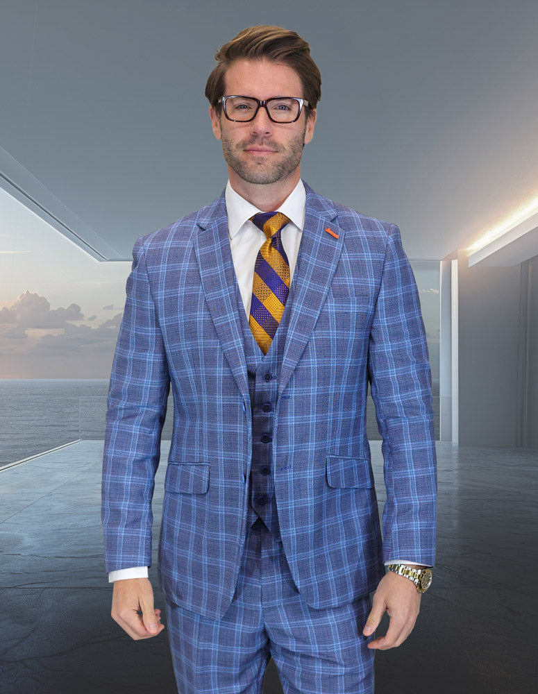 A man in glasses wears the Statement Clothing ZILONI-5-INDIGO modern fit Italian Super 200's wool suit with a yellow and purple striped tie, standing indoors by large windows with a seascape view.
