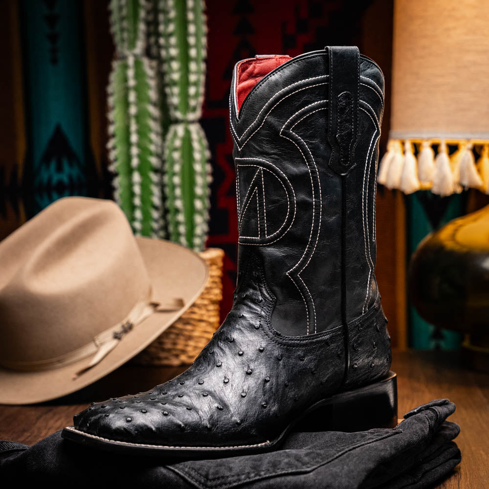 The Alabama Black by Marco Di Milano: a pair of black ostrich skin cowboy boots with white stitching, shown from side and sole views. These luxury men's boots combine classic western style with superb craftsmanship.