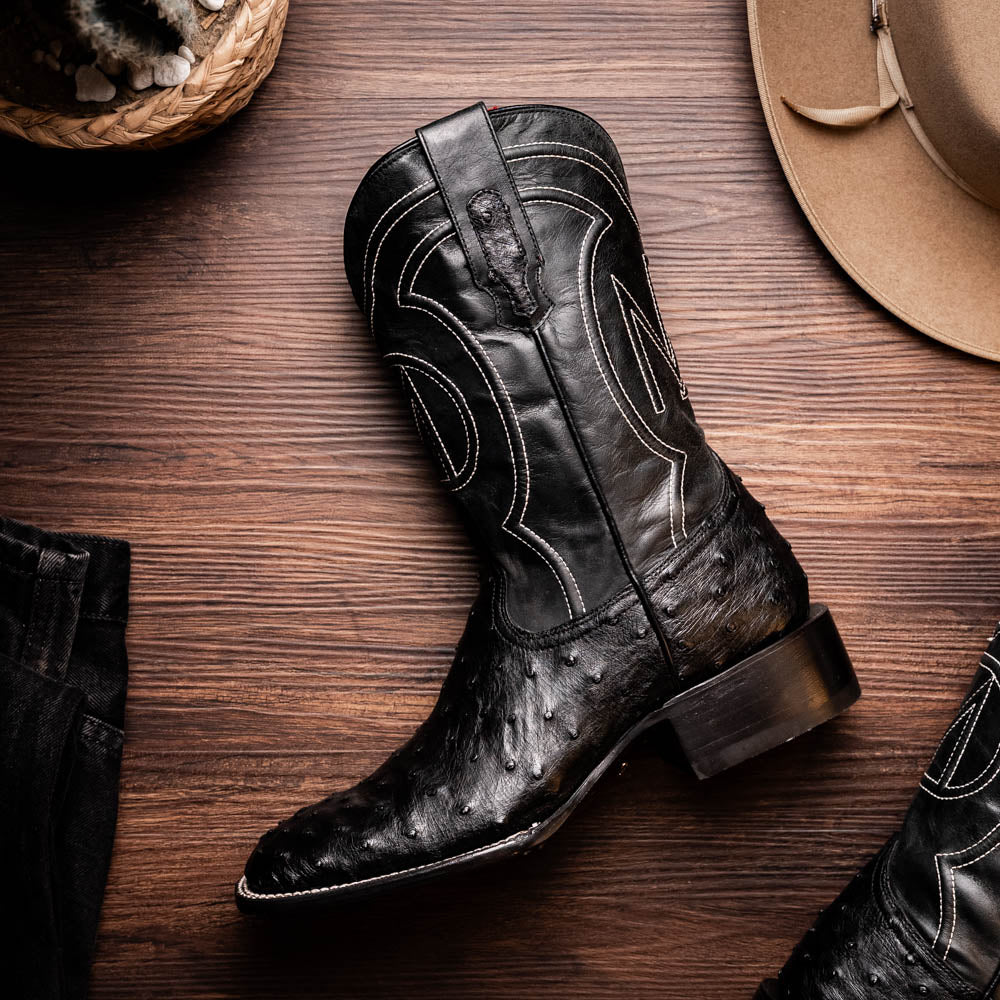 The Alabama Black by Marco Di Milano: a pair of black ostrich skin cowboy boots with white stitching, shown from side and sole views. These luxury men's boots combine classic western style with superb craftsmanship.