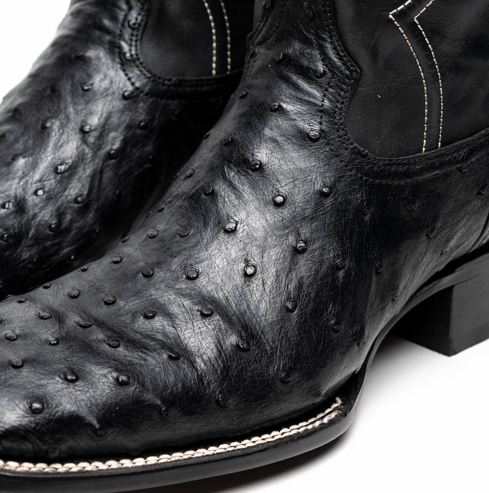 The Alabama Black by Marco Di Milano: a pair of black ostrich skin cowboy boots with white stitching, shown from side and sole views. These luxury men's boots combine classic western style with superb craftsmanship.