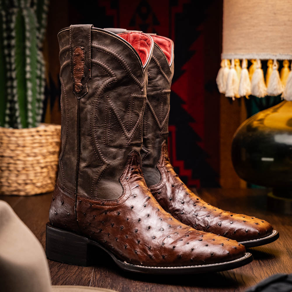 A pair of Marco Di Milano Alabama Kango Tabac men’s boots, handcrafted with genuine ostrich skin foot and dark upper, one upright and one displaying the branded sole, showcase classic Western cowboy style.