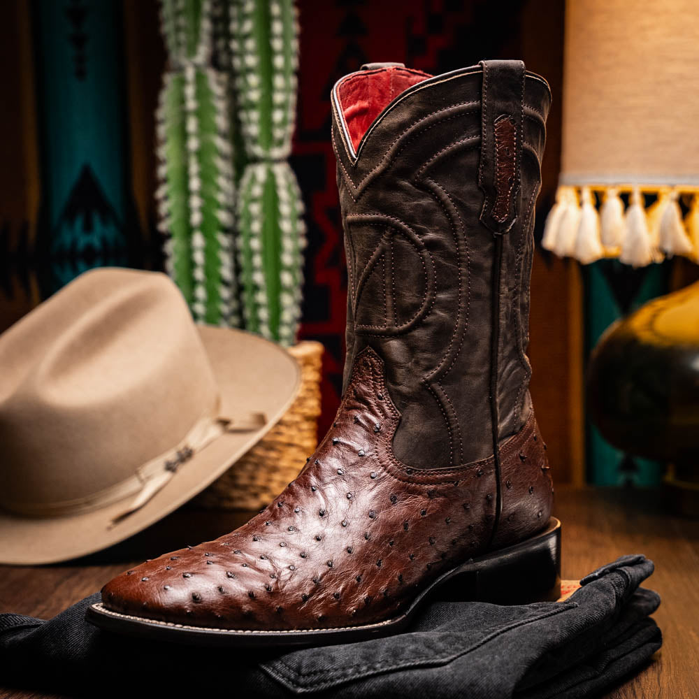 A pair of Marco Di Milano Alabama Kango Tabac men’s boots, handcrafted with genuine ostrich skin foot and dark upper, one upright and one displaying the branded sole, showcase classic Western cowboy style.