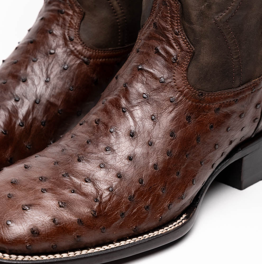 A pair of Marco Di Milano Alabama Kango Tabac men’s boots, handcrafted with genuine ostrich skin foot and dark upper, one upright and one displaying the branded sole, showcase classic Western cowboy style.