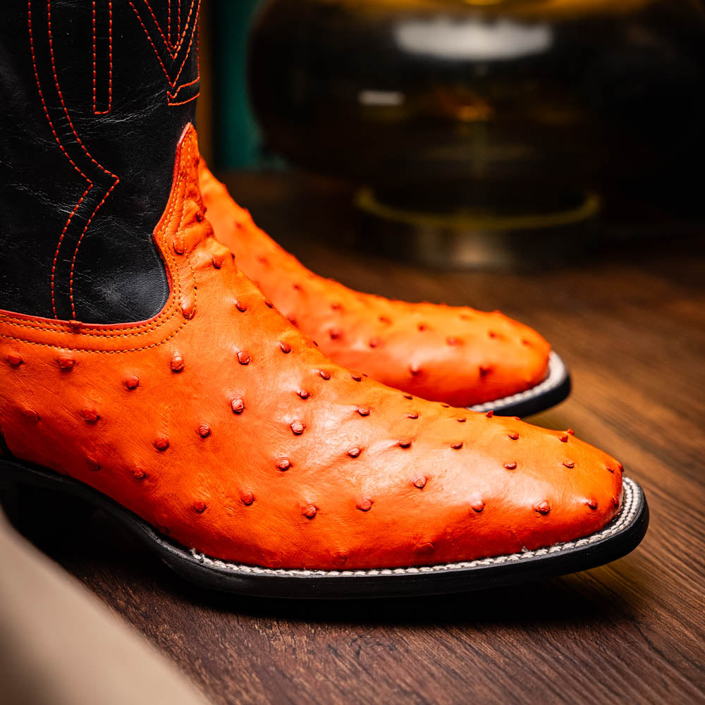 A pair of Alabama Orange cowboy boots by Marco Di Milano featuring a textured orange and black genuine ostrich upper and a visible logo on the leather sole.