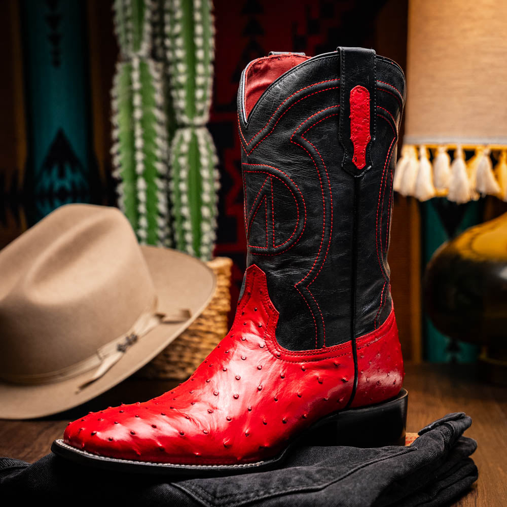 The Marco Di Milano Alabama Red boots feature handcrafted red and black textured leather; one stands upright while the other reveals the branded sole—a modern take on classic Western style.