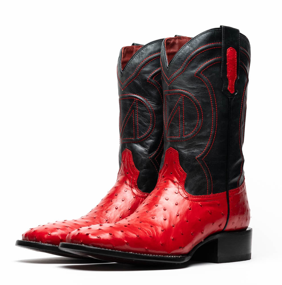 The Marco Di Milano Alabama Red boots feature handcrafted red and black textured leather; one stands upright while the other reveals the branded sole—a modern take on classic Western style.