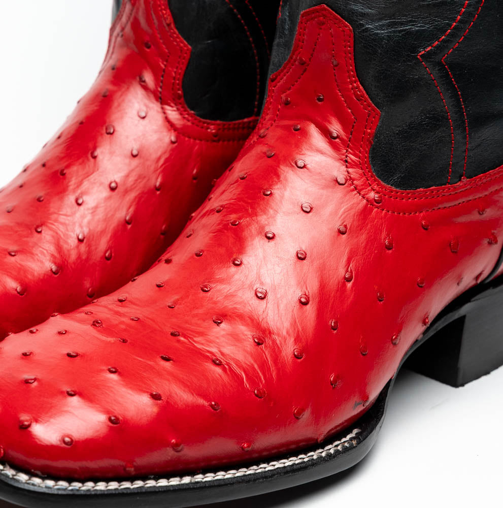 The Marco Di Milano Alabama Red boots feature handcrafted red and black textured leather; one stands upright while the other reveals the branded sole—a modern take on classic Western style.