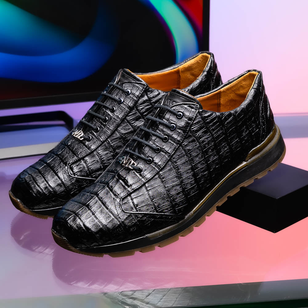 The Alonzo Black by Marco Di Milano: luxury men's sneakers crafted from black genuine caiman crocodile leather with a hand-painted finish and brown rubber soles—one shoe upright, the other leaning against it.