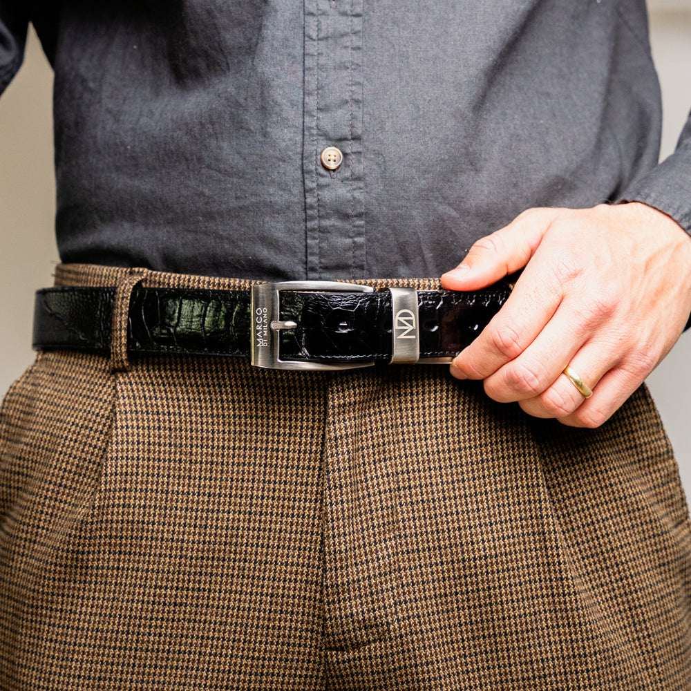 Alessio Belt Black by Marco Di Milano—a handcrafted leather belt in black with a textured finish and a silver buckle engraved with “ATELIER MILANO.” The belt is artfully coiled in a loose loop against a white background.