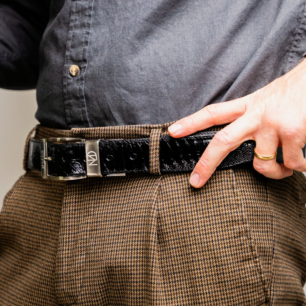 Alessio Belt Black by Marco Di Milano—a handcrafted leather belt in black with a textured finish and a silver buckle engraved with “ATELIER MILANO.” The belt is artfully coiled in a loose loop against a white background.