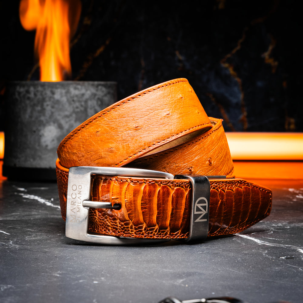 A coiled Alessio Belt Cognac by Marco Di Milano, crafted from genuine ostrich leather in light brown with a textured pattern and a silver buckle engraved with the brand name.